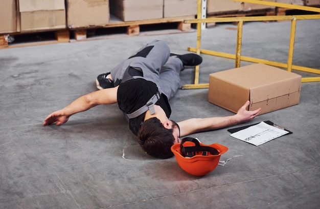 Photo warehouse worker after an accident in the storage man in uniform lying down on the ground