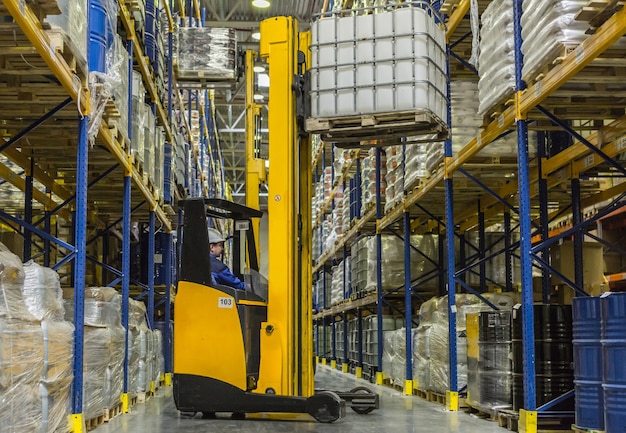 Warehouse worker on stacker loading cargo on shelf