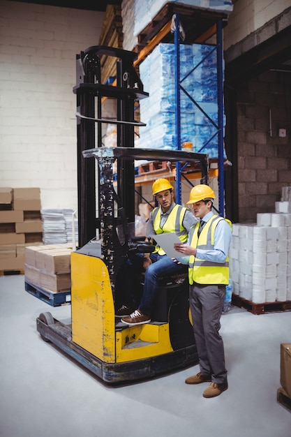 Warehouse worker talking with forklift driver in warehouse