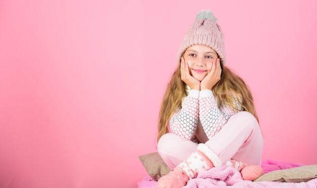 Warm clothes concept Keep warm and comfortable Warm accessories that will keep you cozy this winter Kid girl wear knitted hat relaxing pink background Child long hair warm woolen hat enjoy warm