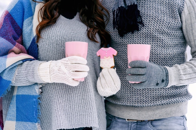 Photo warm dressed hands of young couple holds pink cups and pink biscuits