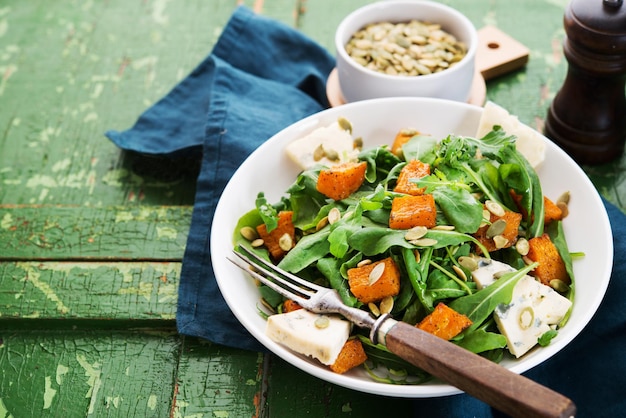 Warm salad with arugula, baked pumpkin, cheese and pumpkin seeds on a rustic background, copy space