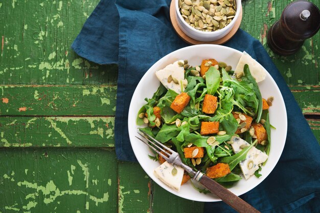 Warm salad with arugula, baked pumpkin, cheese and pumpkin seeds on a rustic background, top view