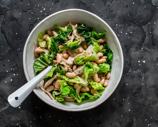 Warm salad with beans baked chicken breast romaine lettuce on a dark background top view