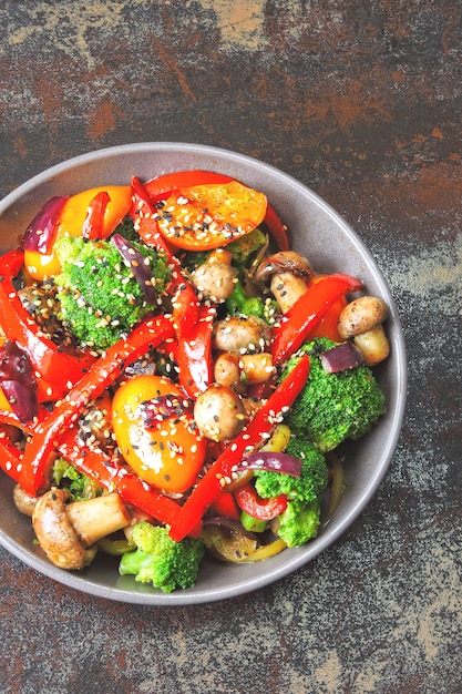 Warm salad with broccoli, mushrooms and red paprika. Vegan bowl with warm vegetables on a stylish shabby background. Healthy food. Fitness lunch with mushrooms and vegetables.