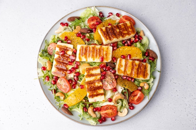 Warm salad with fried halloumi cheese nuts cashews and almonds cherry tomatoes pomegranate orange and arugula Traditional cheese of the Eastern Mediterranean Selective focus closeup top view