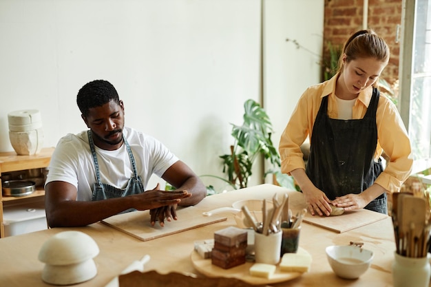 Warm toned portrait of young black man shaping clay while enjoying art class in pottery studio with