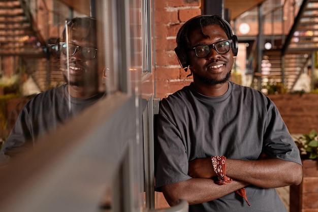 Warm toned waist up portrait of young black man wearing headphones and listening to music while lean