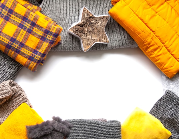 Warm winter wear on white background. Copy space. Yellow and grey trendy fashion colors. Knitted jumpers, jackets, mittens and plaids.