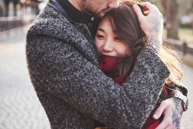 Warming by using red plaid. Happy multiracial couple together outdoors in the city. Asian girl with her caucasian boyfriend.