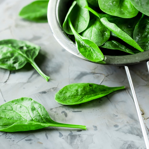 Washed spinach in a metal colander on a gray background