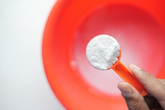 Washing powder in plastic spoon on blue background