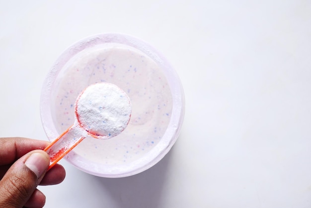 Washing powder in plastic spoon on white background with copy space