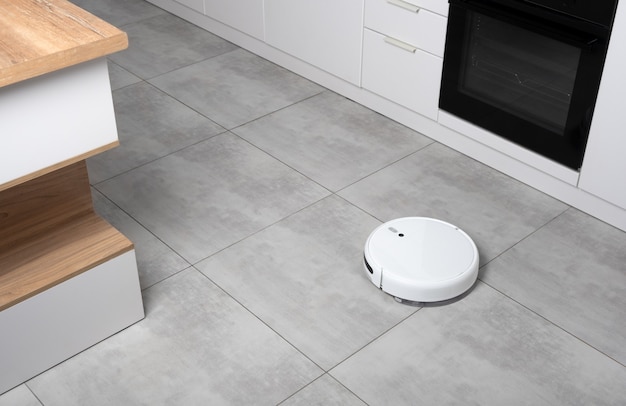 Photo washing white robot vacuum cleaner on a concrete tile floor cleaning dust in a scandinavian loft minimalist kitchen interior. smart electronic household technology