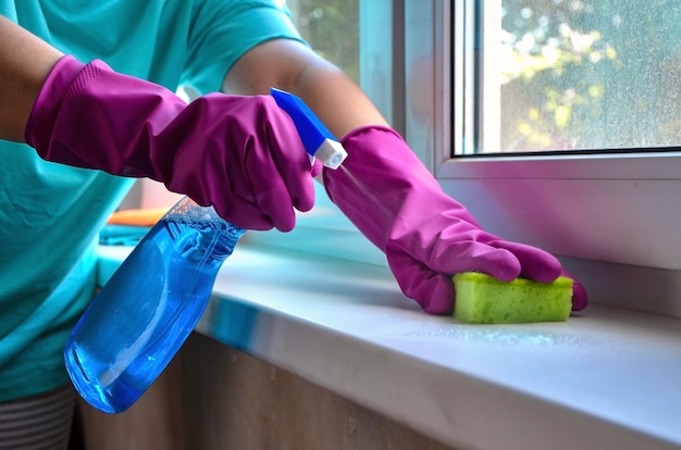 Washing windows. Female hands in gloves hold spray bottle with glass cleaner and sponge.