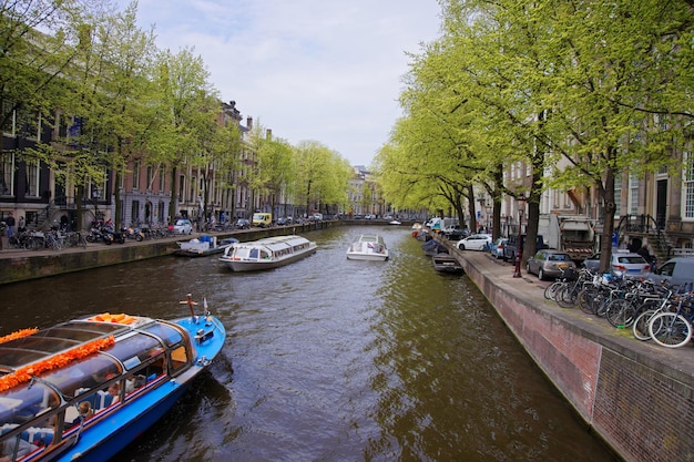 Water boats on canal of Amstel River and buildings at embankment of Amsterdam, Netherlands.