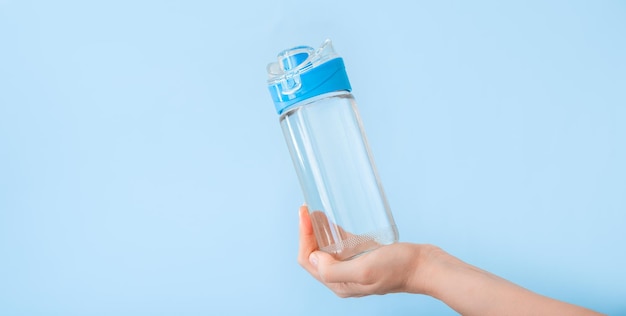 Water bottle in female hand. Reusable drinking water bottle for sports on blue backgraund. Healthy lifestyle and fitness concept. Long web banner with copy space.