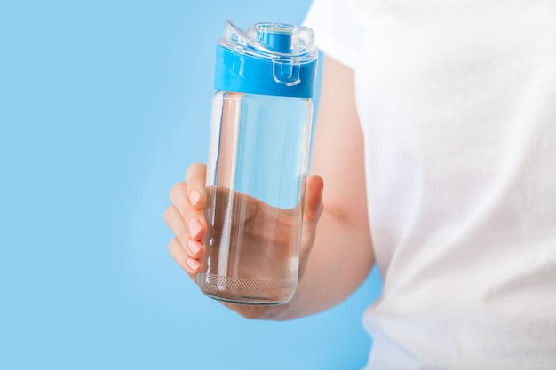 Water bottle in female hand. Reusable drinking water bottle for sports on blue backgraund. Healthy lifestyle and fitness concept.