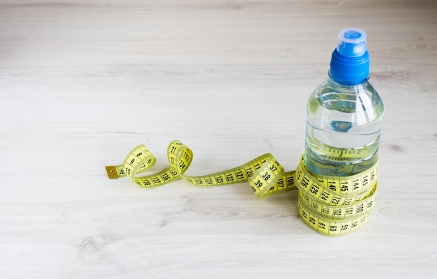 Water bottle with measuring tape on a wooden background