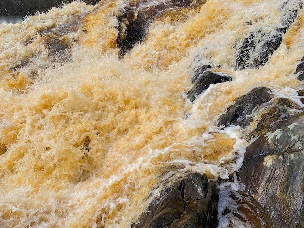 Water brown yellow flowing bubbling foaming stream through rocks protruding from the water high qual