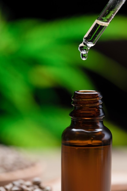 Water drop of CBD oil on tip of dropper close to bottle with legalized hemp leaf