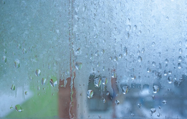 Water droplets condensation background of dew on glass humidity and foggy blank background Condensation on the glass of metalplastic window Outside the window bad weather rain