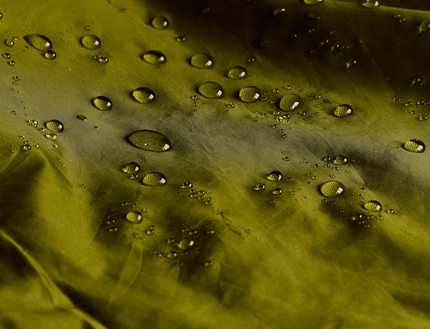 Water drops on waterproof membrane fabric. Detail view of texture of olive waterproof cloth.