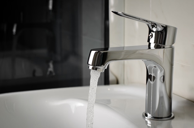 Water flows from the tap or faucet in bathroom. Copy space, close up