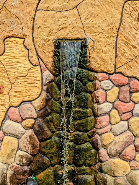 A water fountain with a stone wall and a green stone wall