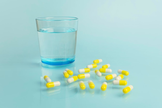 Water glass white and yellow tablets on blue background Health and medicine Copy space