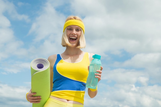 Photo water and hydration concept sport activity outdoor blonde cheerful smiling woman holding sport yoga ...