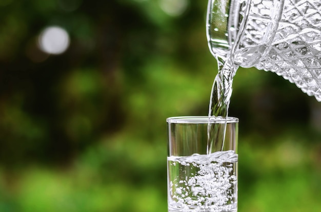 Water  into glass on green nature background