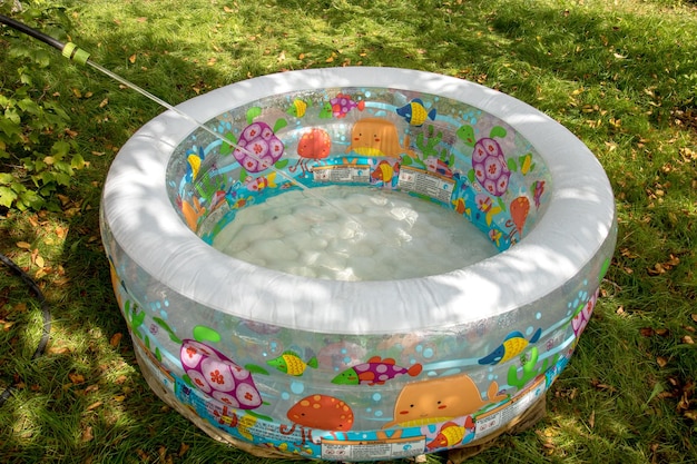 Water is poured from a hose into an inflatable children's pool standing on the grass