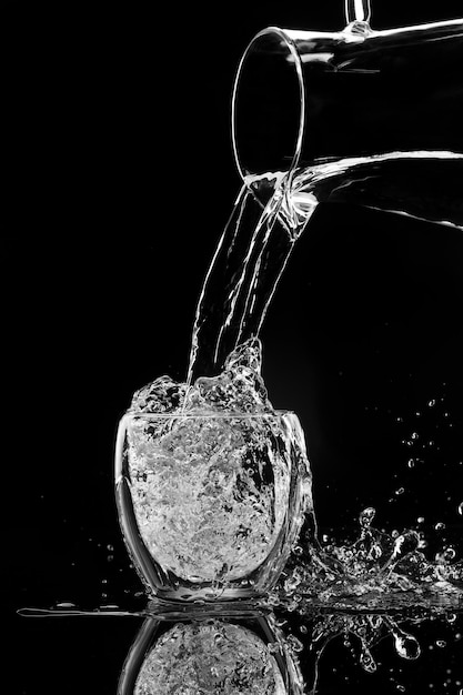 Water pours into a glass from a decanter on black background