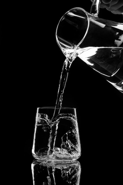 Water pours into a glass from a decanter on black background