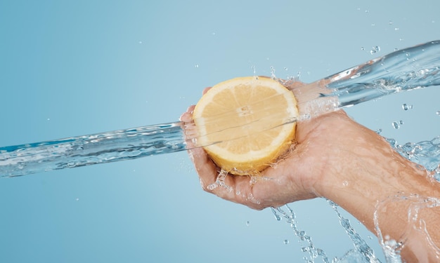 Water splash and beauty with hands and lemon for health wellness and hydration Vitamin c refreshing or nutrition with citrus fruits and model against blue background for natural vitality or diet