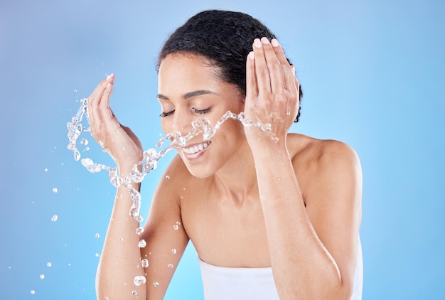 Water splash and skincare woman in studio for face cleaning morning wellness and healthy glow with blue background for advertising space Beauty model with water in hands for facial cosmetic wash