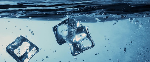 Water splashing and ice cube Ice splashing into a glass of water Underwater pouring ice cubes falling into clear watering background Refreshing chill drinking Ices in a glass with blue background