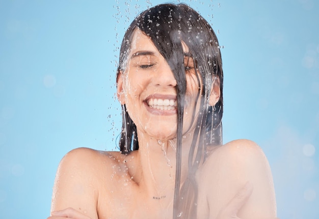 Water steam and cleaning with a woman in the shower in studio on a blue background for hygiene or hydration Skincare relax and smile with a model female washing her face in the bathroom for health