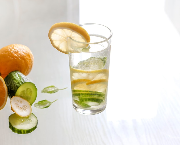 Water with lemon and cucumber in a glass on a light background.Detox drink.