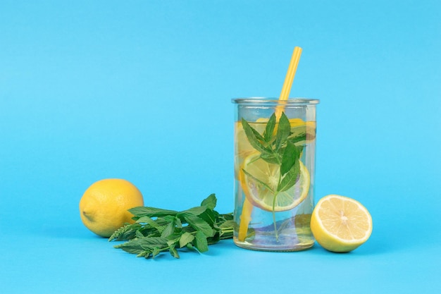 Photo water with lemon and mint in a glass with a cocktail tube on a blue background