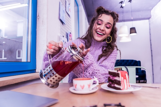 Photo watercolor hearts. laughing positive lady pouring warming tea in pretty cup while sitting at the table