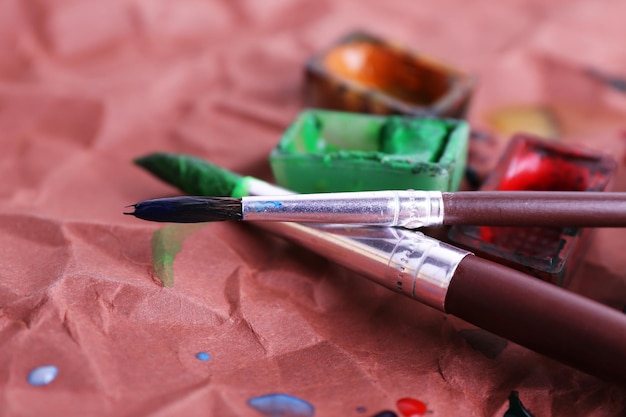 Watercolor paint cubes with brushes and spilled paint on brown paper background