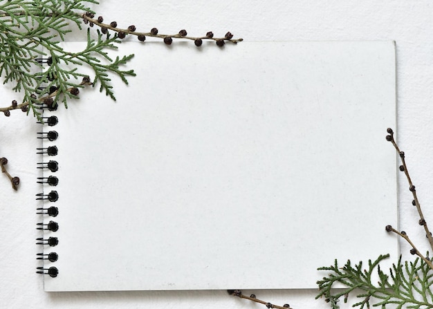 Watercolor white sketchbook on a black spring lying on a linen tablecloth with sprigs of green thuja