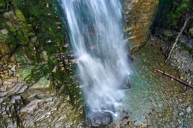 Waterfall on mountain river with white foamy water falling down from rocky formation in summer forest