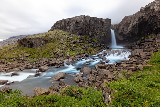 Waterfall in a rocky country with green bushes around in iceland