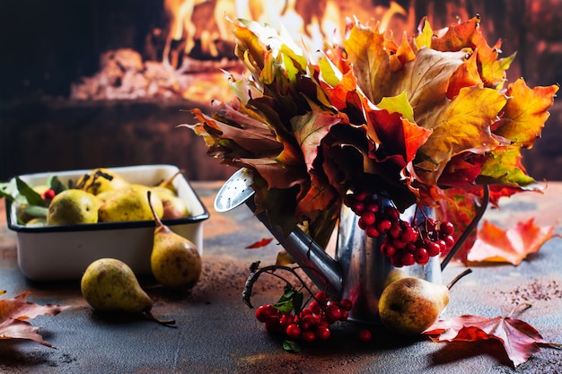 Watering can with autumn leaves and ripe pears near fireplace