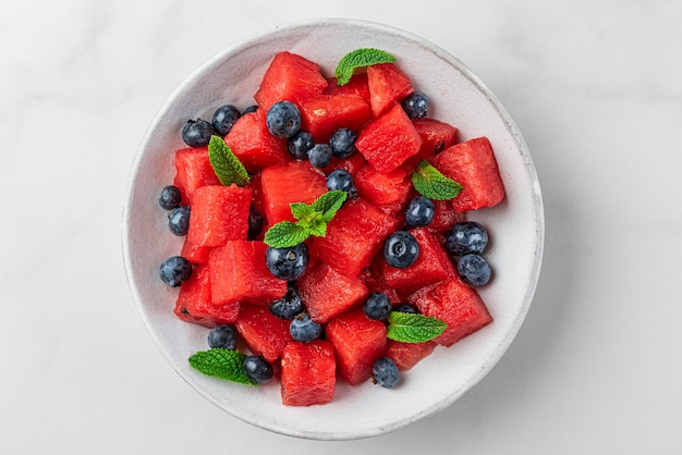 Watermelon and blueberry fruit salad with mint in a plate on white background. Top view. Refreshing summer food