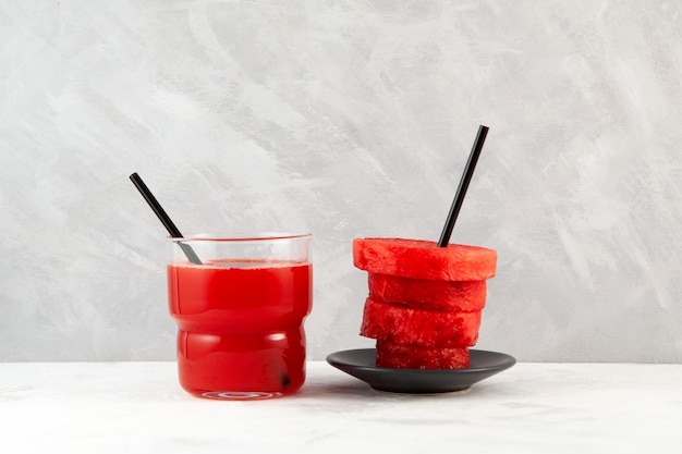 Watermelon fresh juice or smoothie in glass and watermelon slices on grey background.