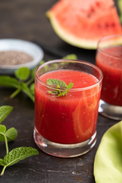 Watermelon juice with chia seeds and mint in glass on a black concrete background with green textile. Healthy drink concept. Side view,  close up, selective focus.